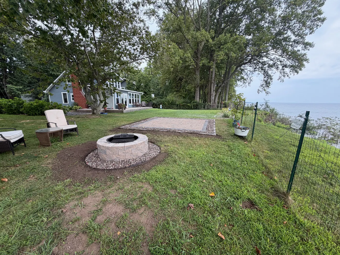 Stone fire pit and paver pad on a lawn overlooking the water