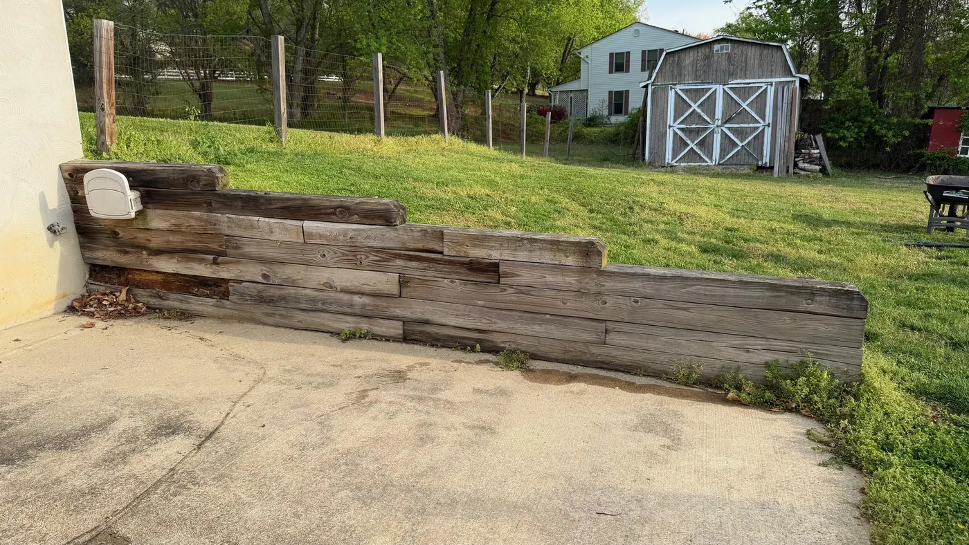 Old timber retaining wall leaning beside a concrete pad